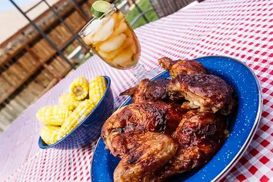 grilled chicken on blute plate corn in blue bowl and ice tea in glass with ice cubes