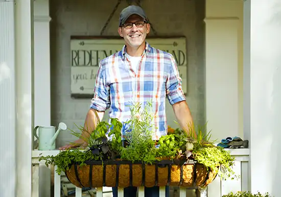 smiling man with herbs hanging in basket from balkony
