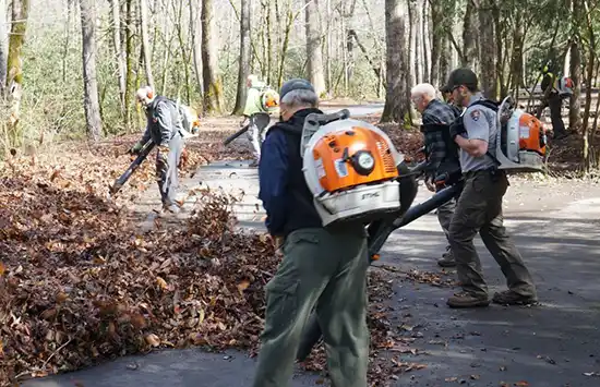 Volunteers and staff use leaf blowers to remove debris