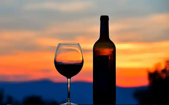 bottle of wine with half full wine glass against blurred blue and orange mountain sunset