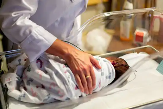 baby in hospital enviroment with woman's hand on his back