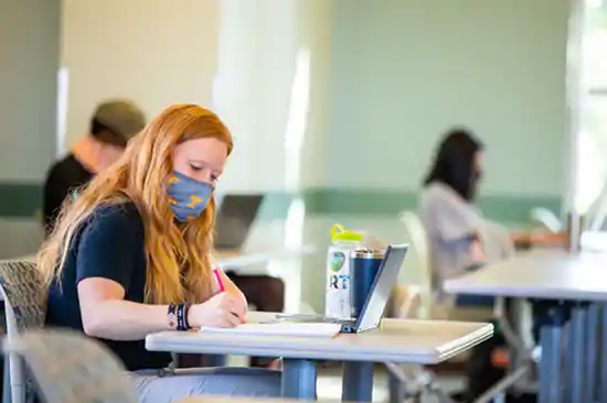 girl with mask in class writing notes