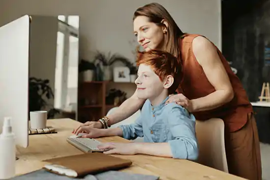 woman in brown outfit watching over shoulder of young boy working on computer
