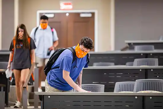 ut student with orange covid mask cleaning class desk