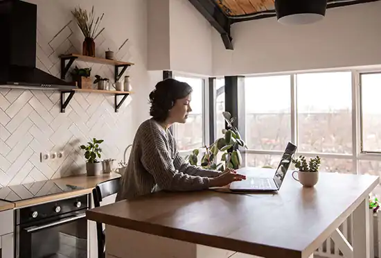 woman working on computer on kitchen table by window