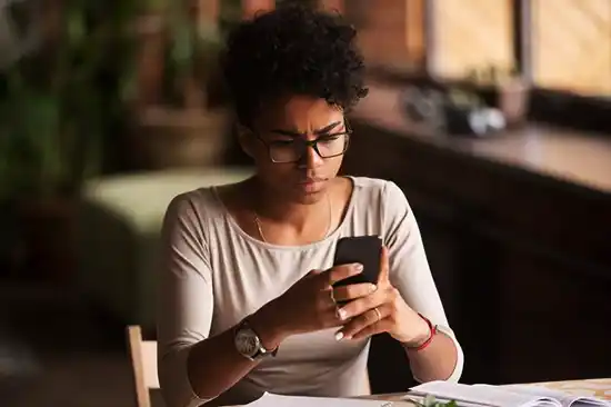 young afro american woman sitting at the table holding cellphone with blurred background